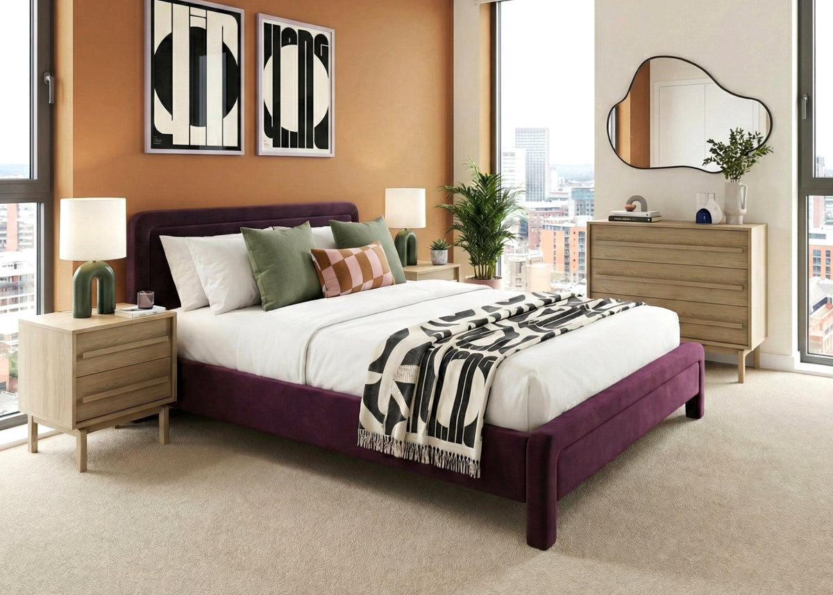 Apartment bedroom with purple bedframe, light wood bedside tables and chest, with orange statement wall