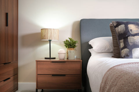 Dark wood bedside table and wardrobe next to grey bed with white wall
