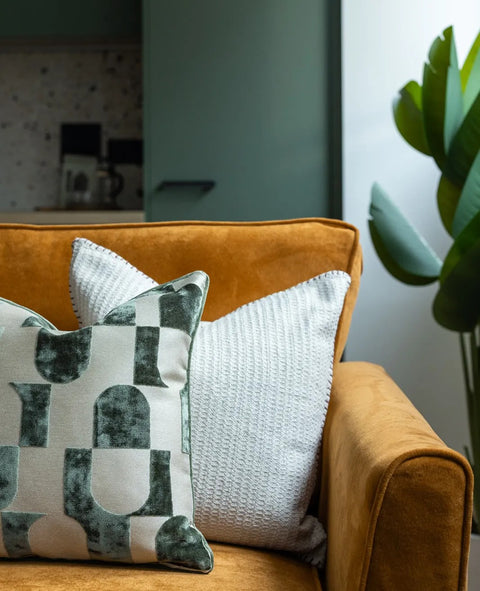Decorative pillows on a mustard sofa with a blurred indoor background