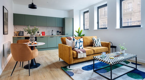 Modern living room with a mustard sofa, coffee table, and kitchen in the background.