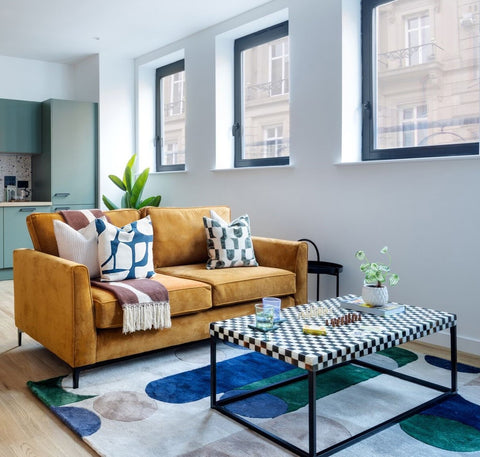Modern living room with a mustard sofa, checkered coffee table, and decorative elements.