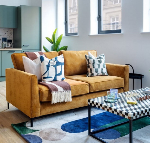 Living room with a mustard sofa, colorful cushions, and a checkered coffee table.
