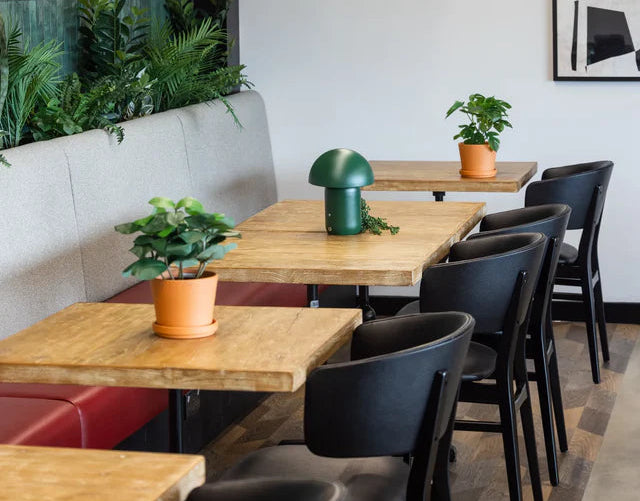Modern restaurant interior with wooden tables, black chairs, and hanging lights.