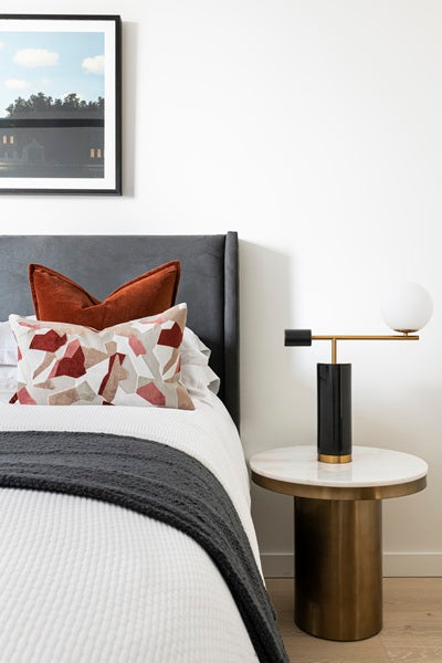 neatly made grey bed with white duvet, gold side table and gold lamp