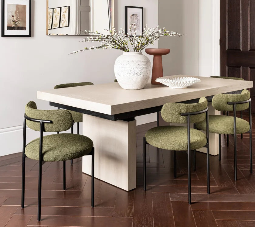 Dining table with six green chairs in a room with framed pictures on the wall.